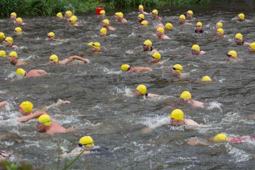 Een groep mensen met gele badmutsen zwemt in een rivier.
