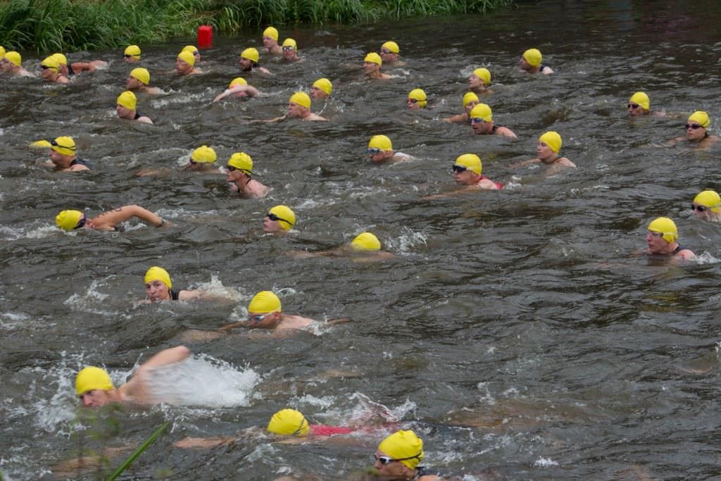 Een groep mensen met gele badmutsen zwemt in een rivier.