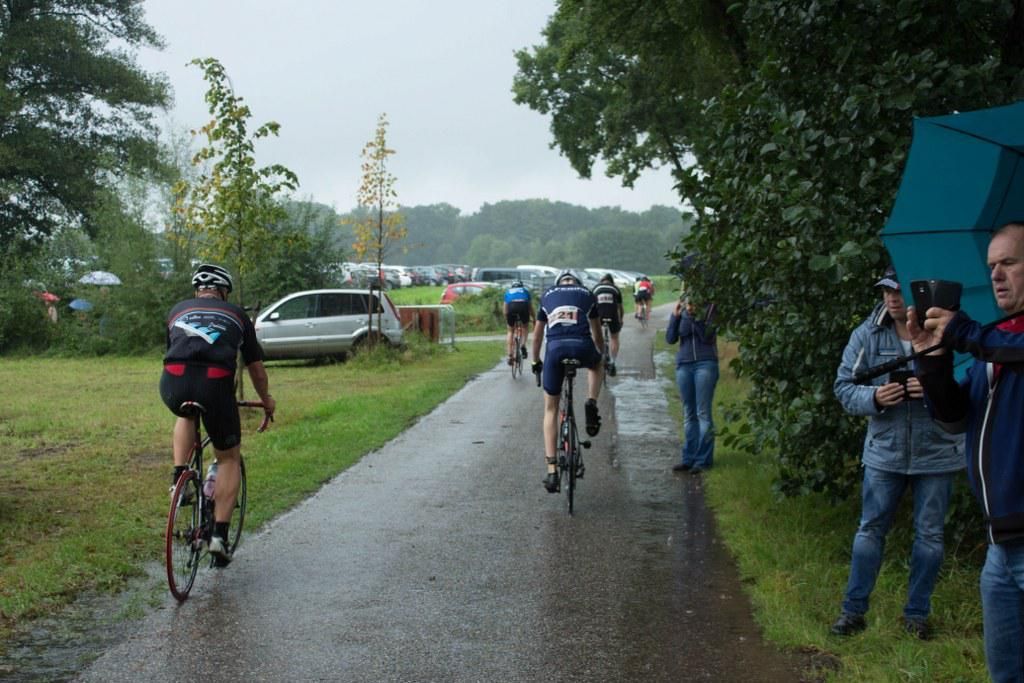 Een groep mensen fietst over een natte weg.