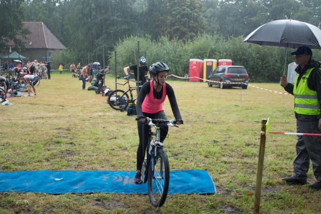Een vrouw fietst in de regen, terwijl een man een paraplu vasthoudt.