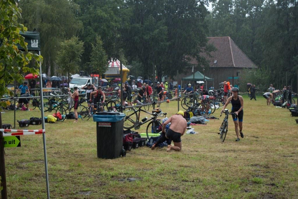 Een groep mensen verzamelt zich op een veld met fietsen en een vuilnisbak.