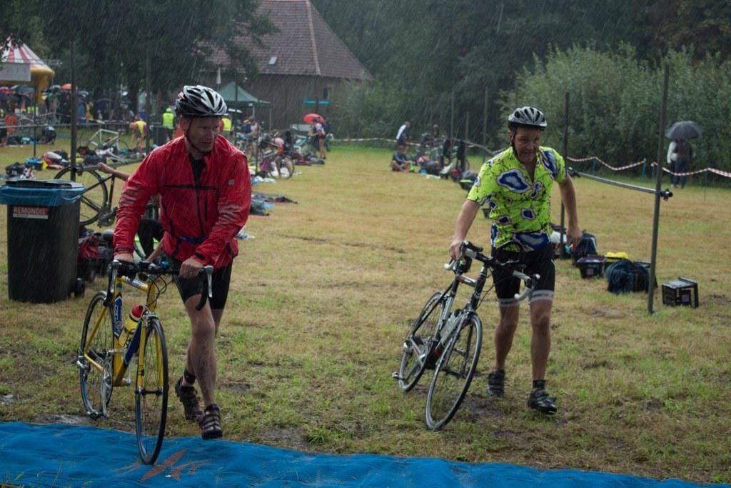 Twee mannen fietsen in de regen in een veld.