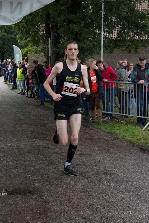 Een man in een zwart tanktopje en korte broek doet mee aan een race.