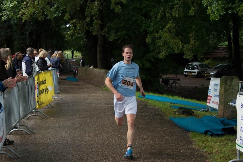 Een man in een blauw shirt en een witte korte broek rent over een pad.