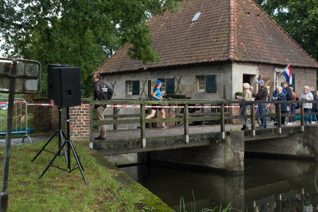 Een groep mensen staat op een brug over een rivier, voor een gebouw.