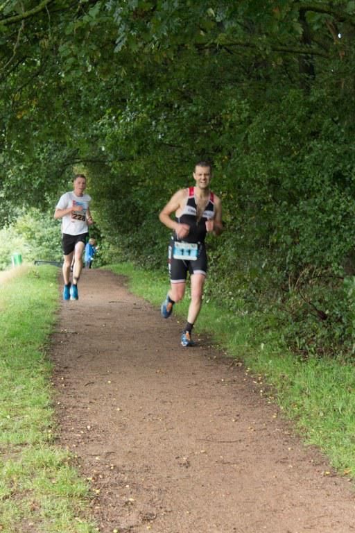 Twee mannen rennen over een zandpad in het bos.