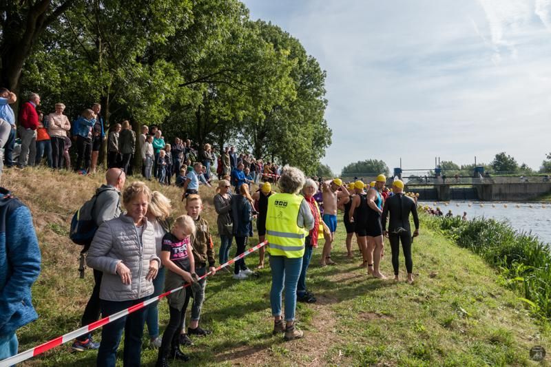Een grote groep mensen staat aan de oever van een rivier.