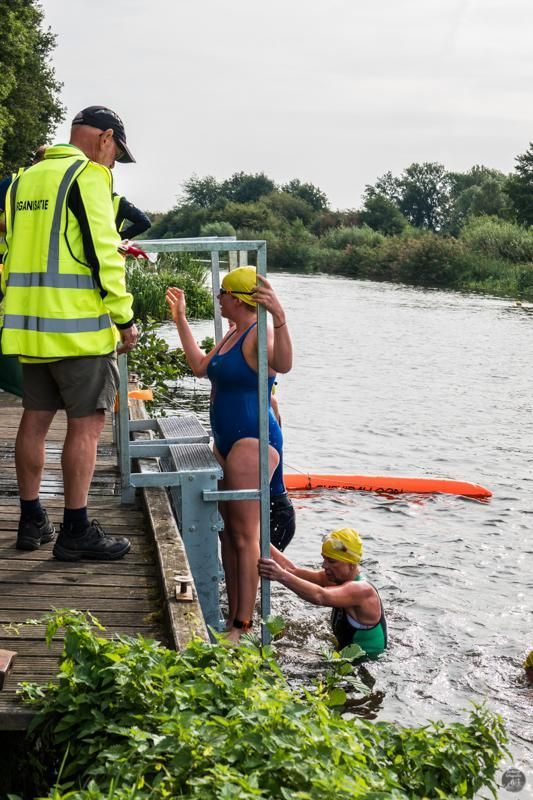 Een man in een geel vest staat naast een vrouw in een blauw badpak in het water.