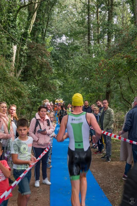Een triatlonloper loopt over een blauw tapijt in het bos.