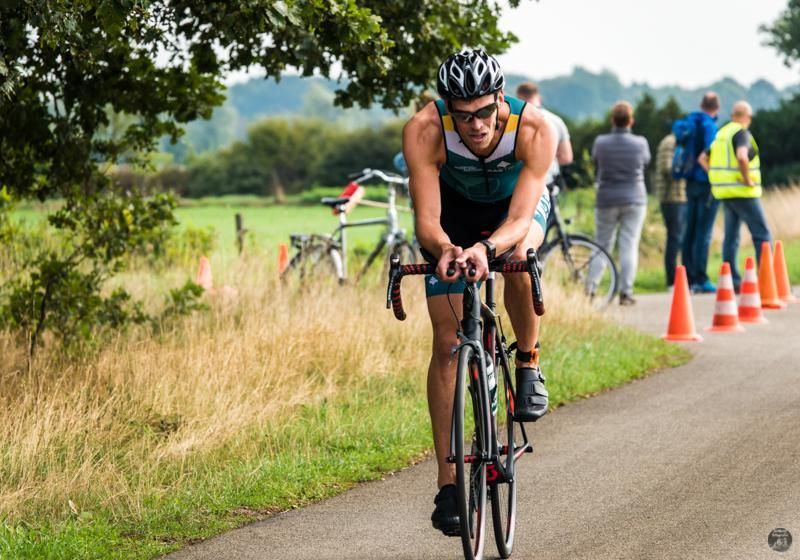 Een man met een helm rijdt op een fiets over de weg.
