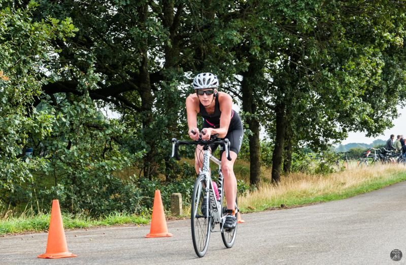 Een vrouw fietst over een weg naast oranje kegels.