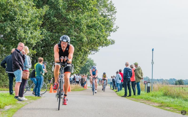 Een man fietst over een weg voor een menigte mensen.