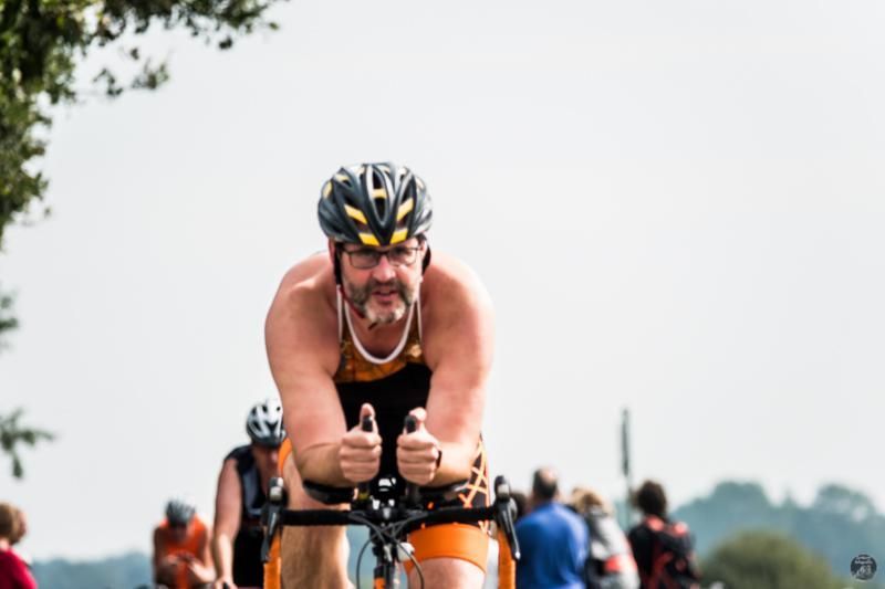 Een man met een helm rijdt op een fiets en steekt zijn duim omhoog.