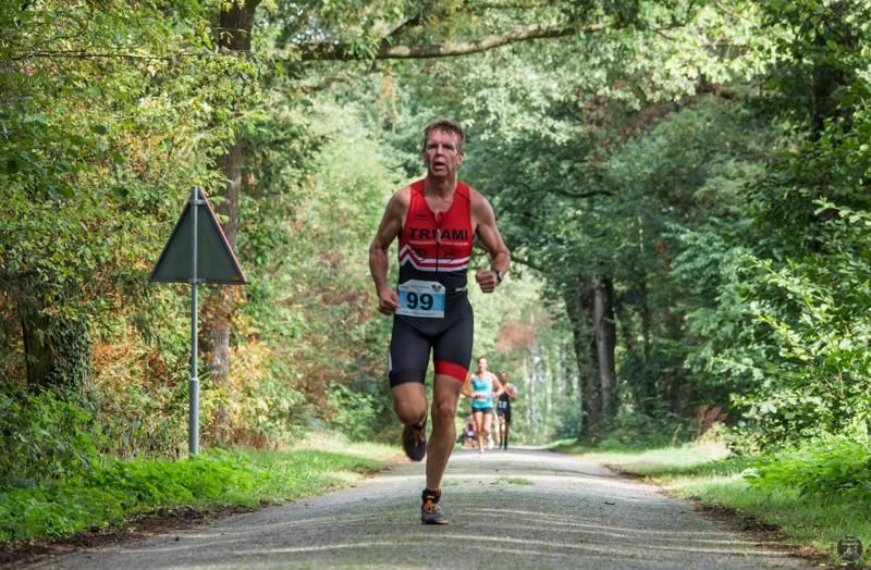 Een man rent over een weg in het bos.