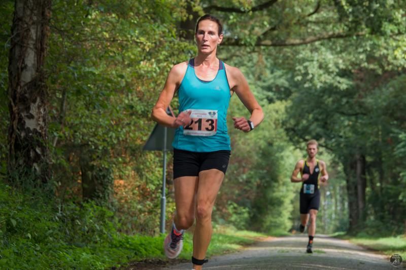 Een vrouw in een blauw tanktopje rent over de weg.