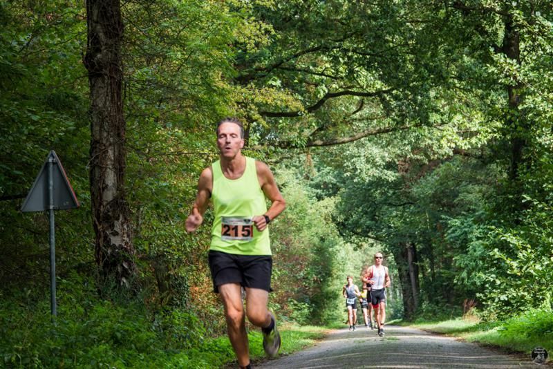 Een man rent over een weg in het bos.