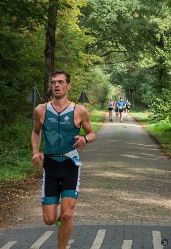 Een man rent over een weg in het bos.