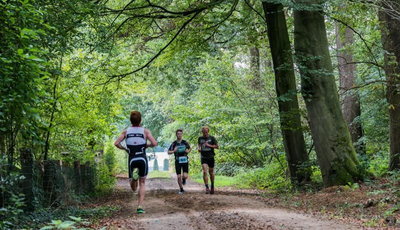 Een groep mensen rent over een onverharde weg in het bos.