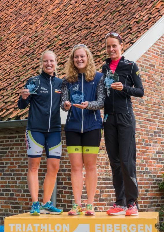 Drie vrouwen staan ​​op een podium met trofeeën in hun handen.