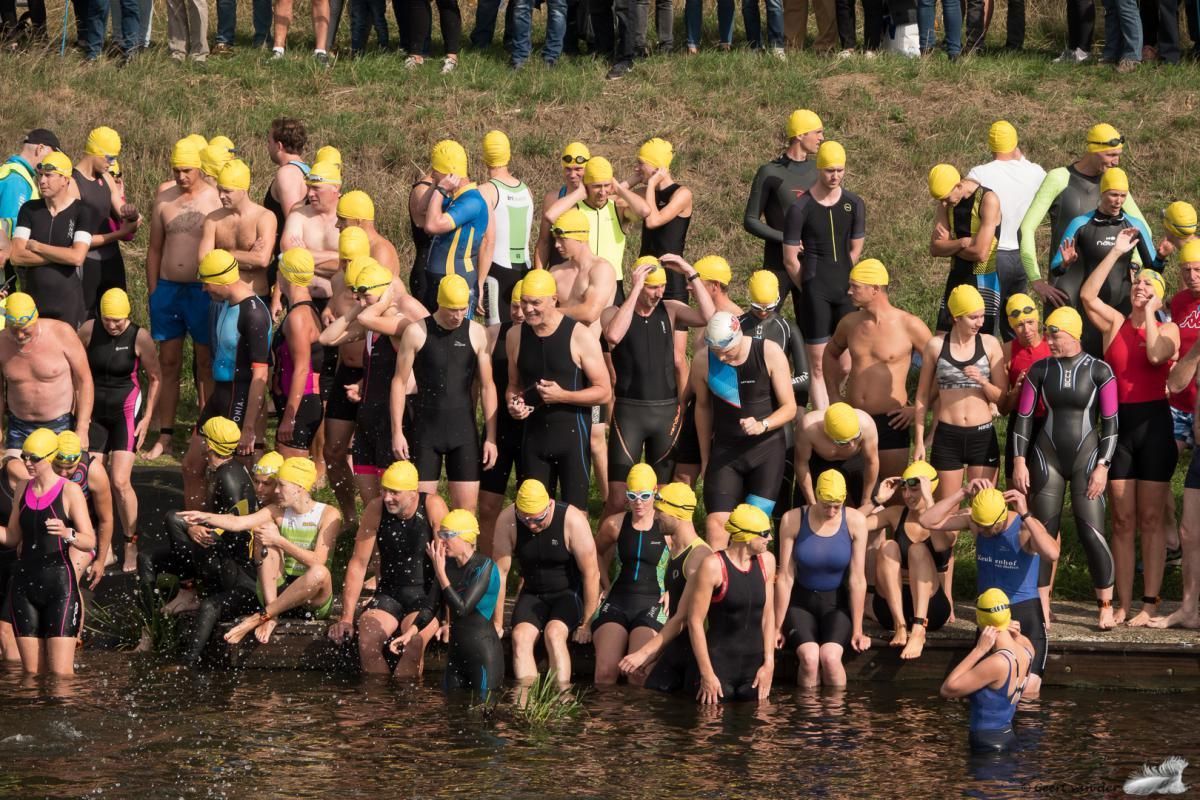 Een groep mensen met wetsuits en badmutsen staat in het water.