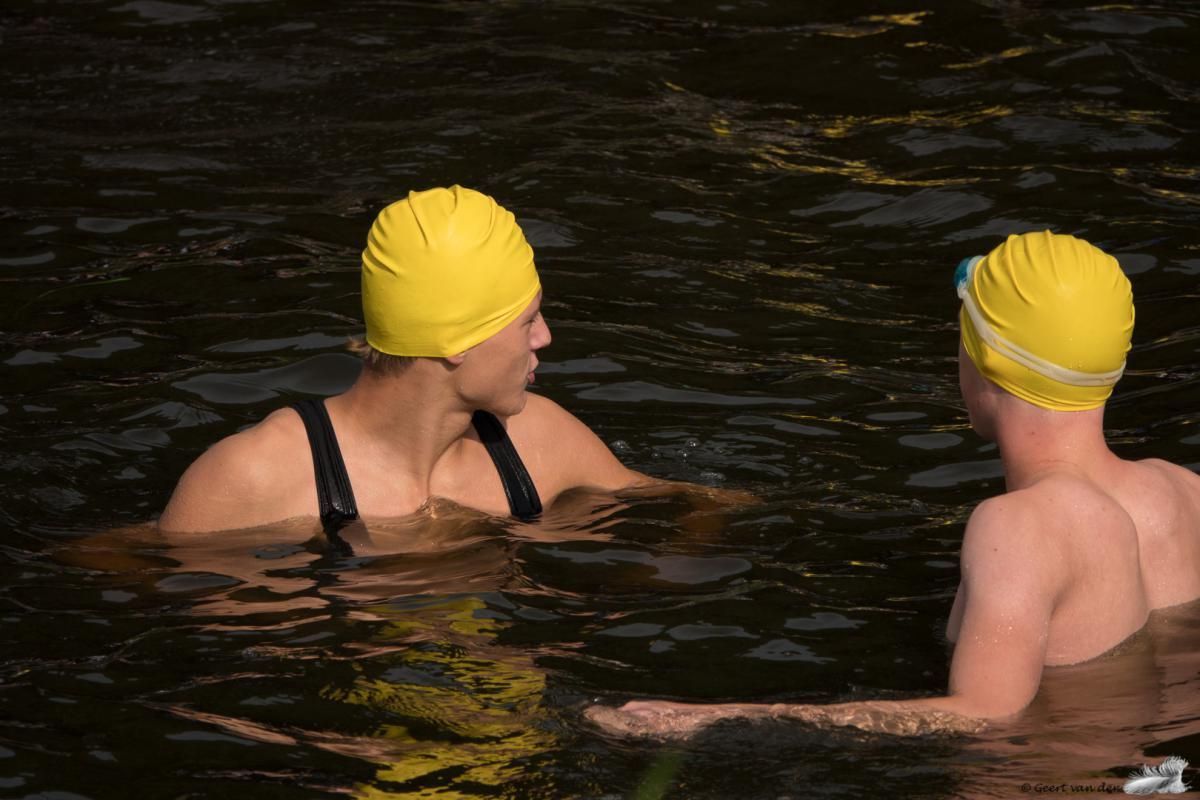 Twee mensen met gele badmutsen praten in het water.