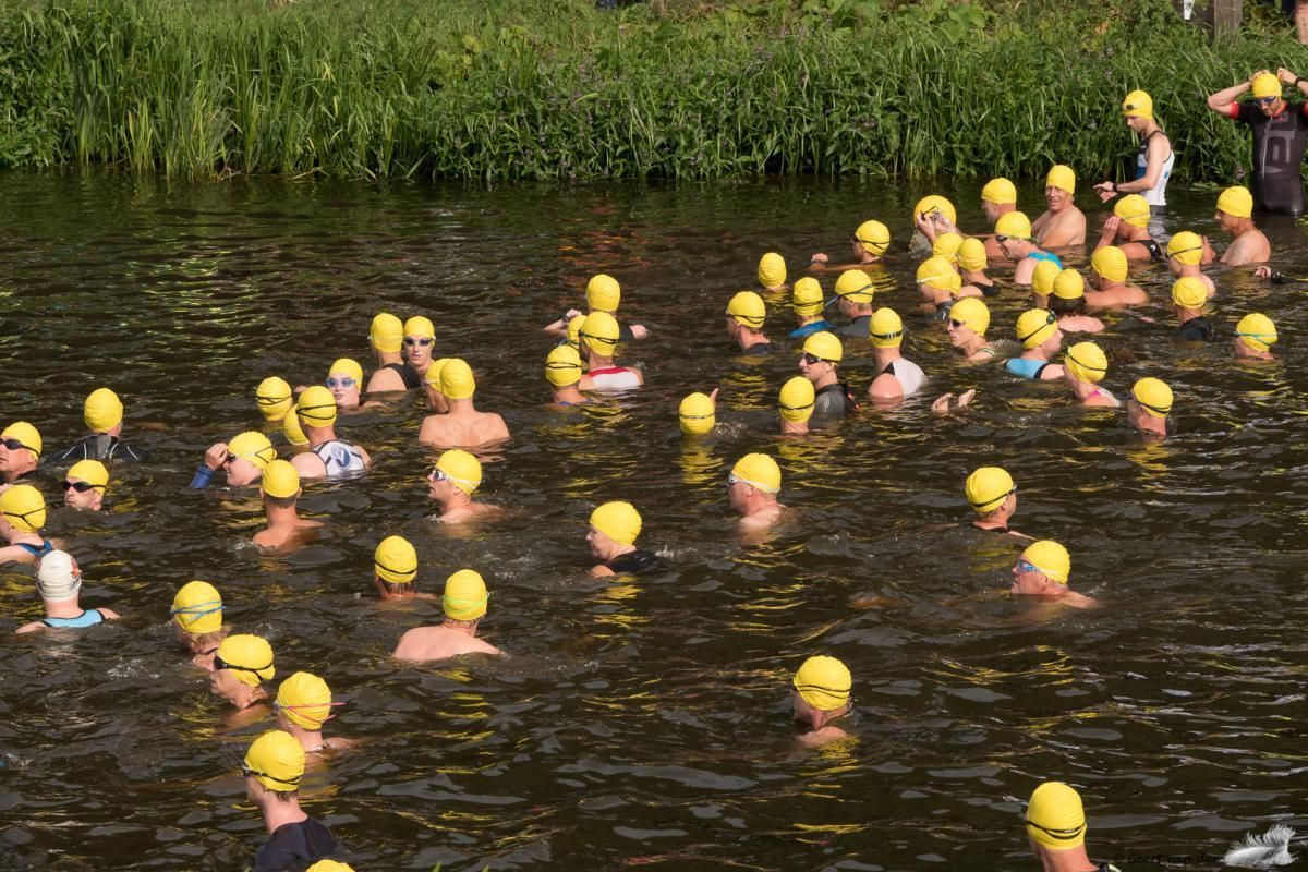 Een groep mensen met gele badmutsen zwemt in een rivier.