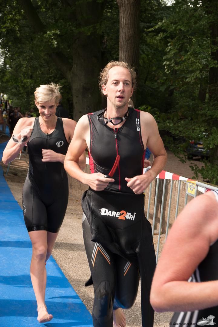 Een man en een vrouw in wetsuits rennen op een blauwe baan.