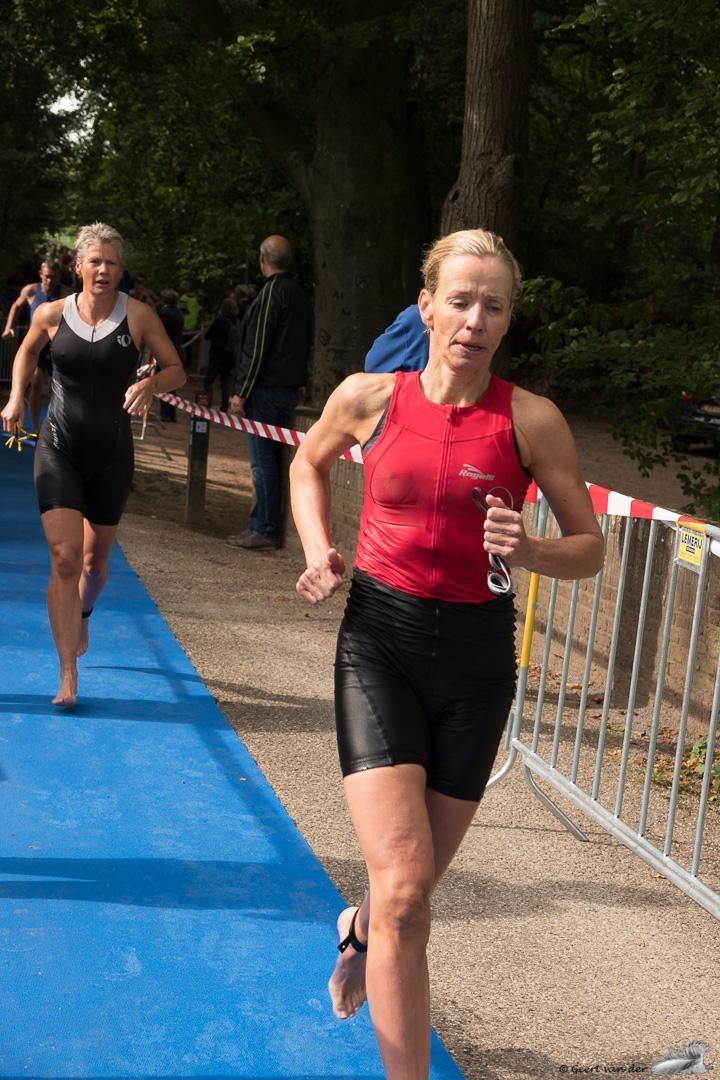 Een vrouw in een rood tanktopje en een zwarte korte broek rent op een blauwe baan.