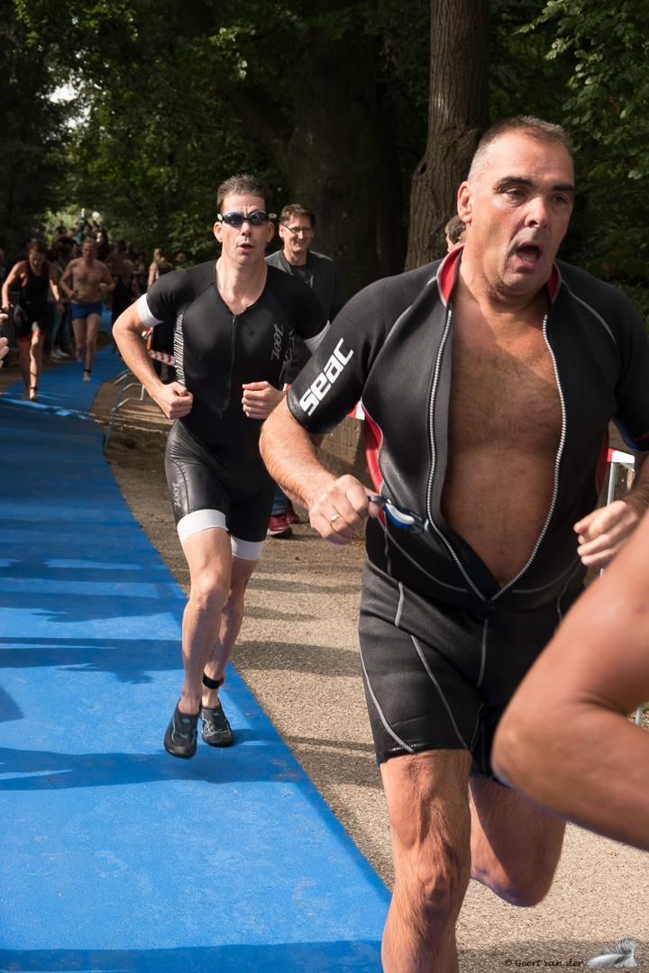 Een man in een wetsuit rent op een blauwe baan