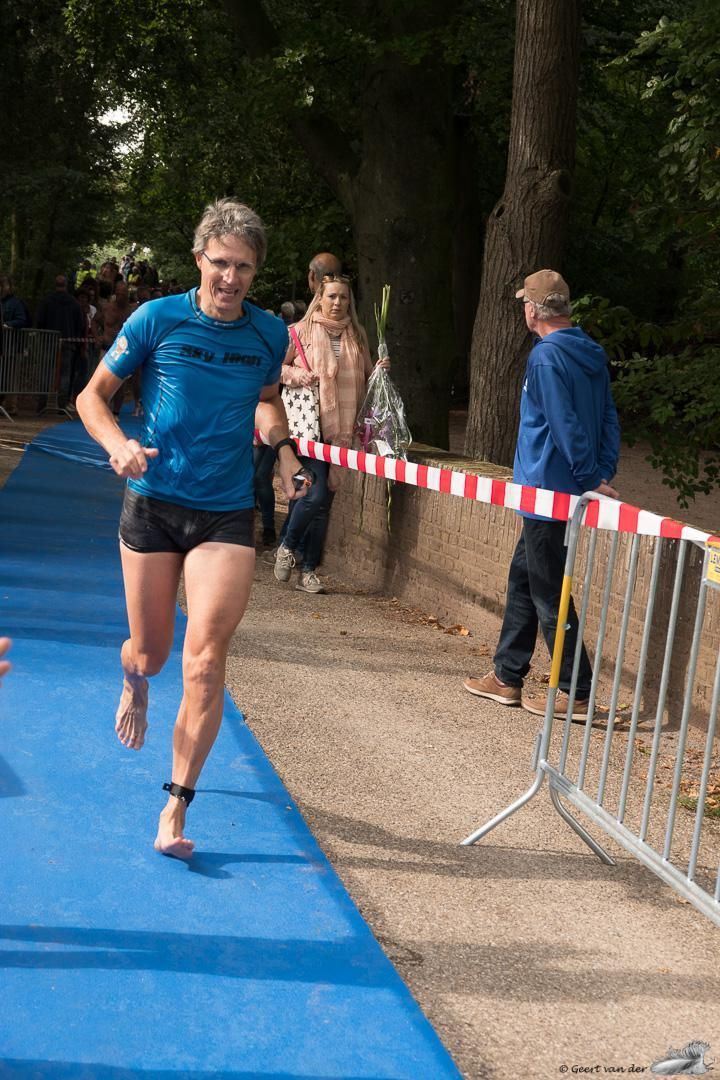 Een man in een blauw shirt en korte broek rent op een blauwe baan.