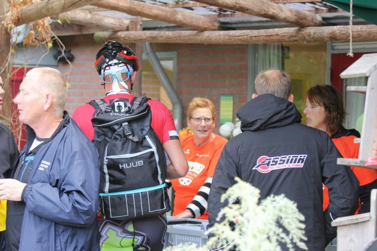 Een groep mensen die voor een gebouw staat, waarvan één man een jas draagt ​​met de tekst assen