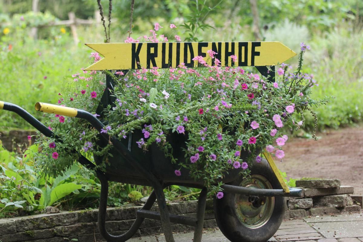 Een kruiwagen vol bloemen en een bordje met de tekst kruidenhof.