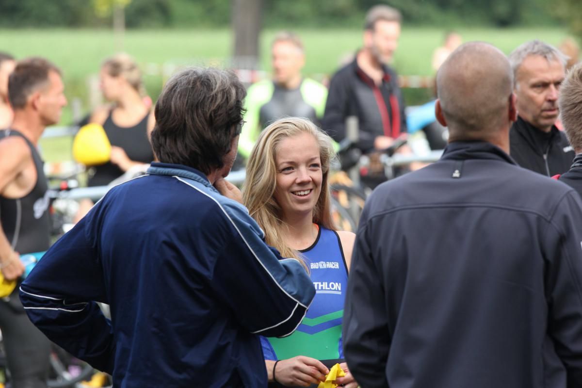 Een vrouw in een blauw en groen tanktopje praat met een man in een zwart jasje