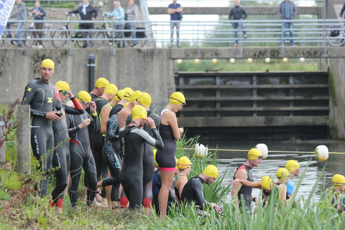 Een groep mensen in wetsuits maakt zich klaar om in een rivier te gaan zwemmen.