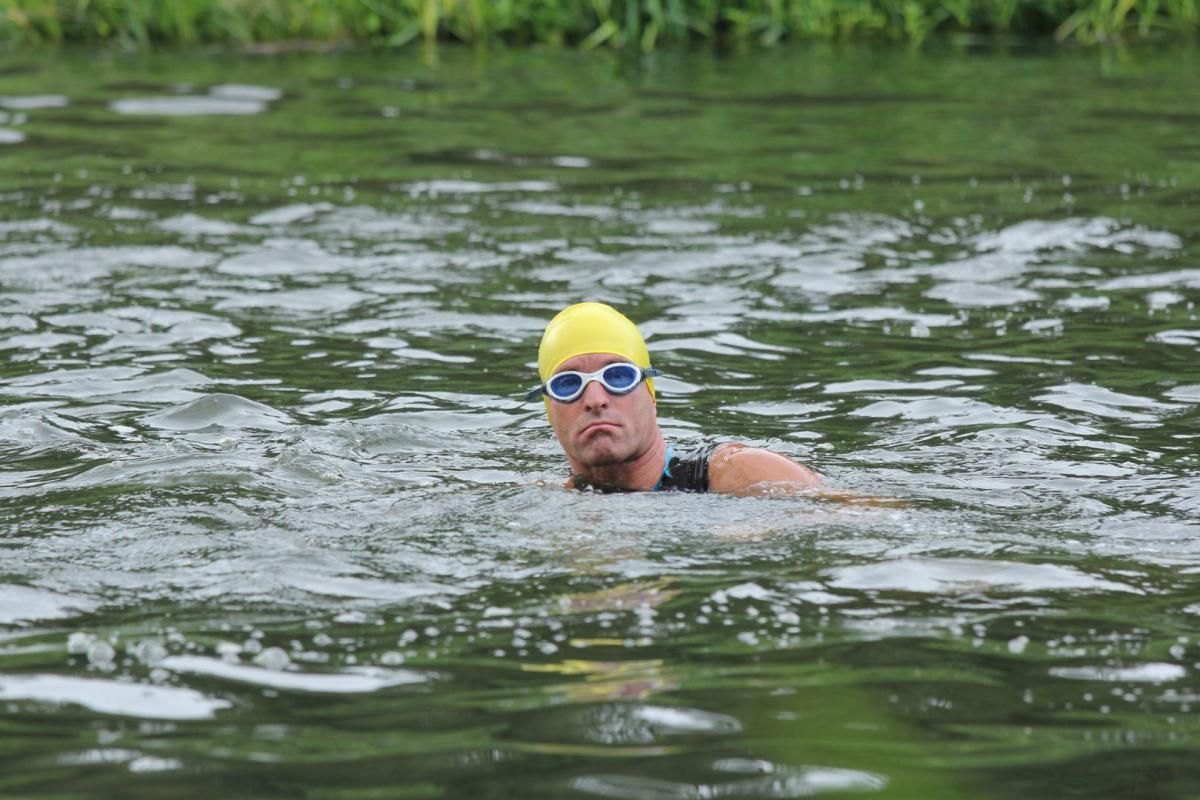 Een man met een gele badmuts en een duikbril zwemt in een meer.