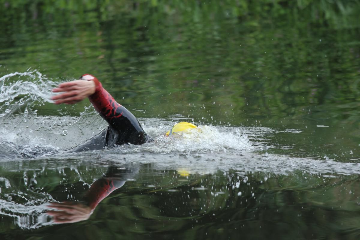 Iemand in een wetsuit zwemt in een meer.