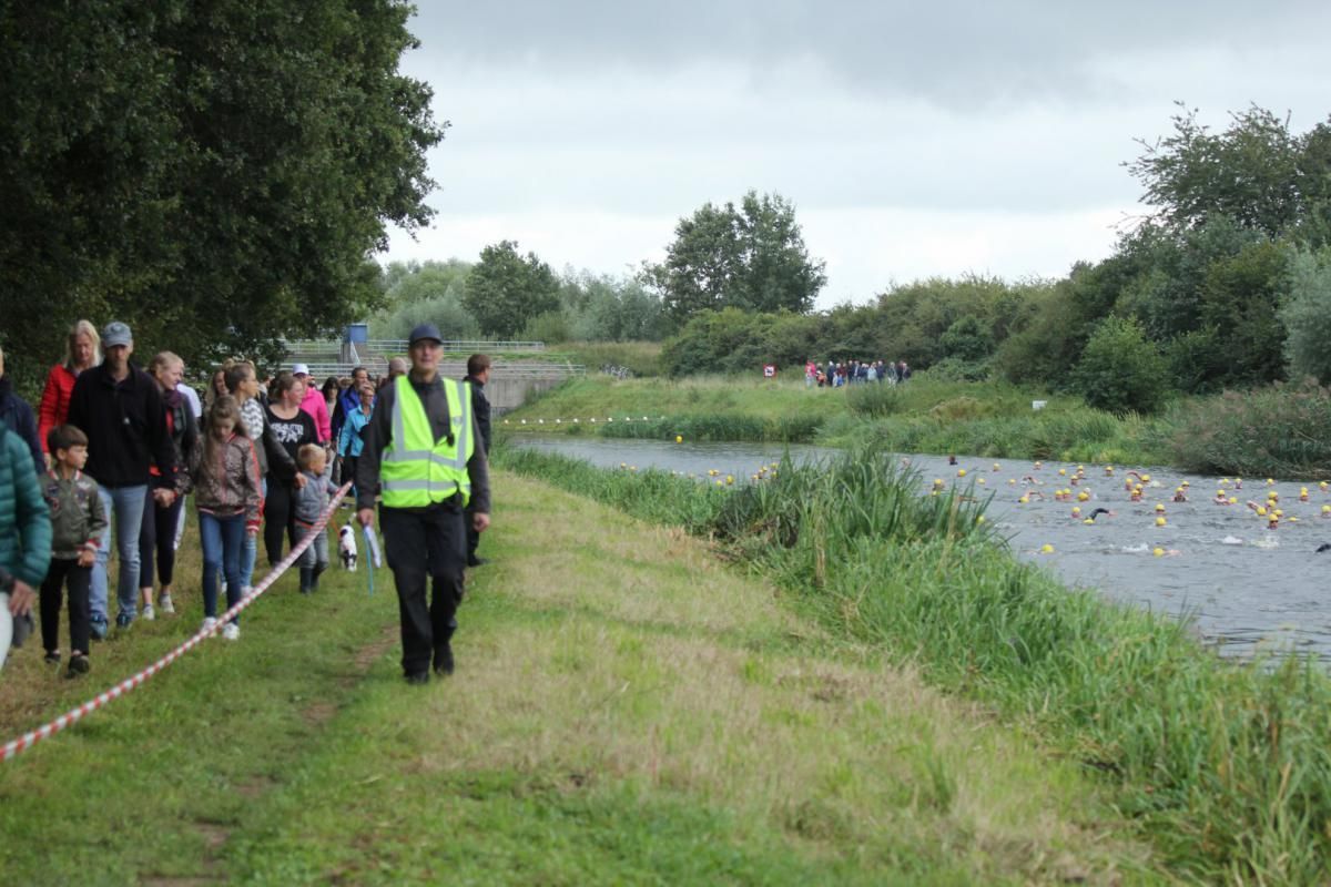 Een groep mensen loopt over een graspad langs een rivier.