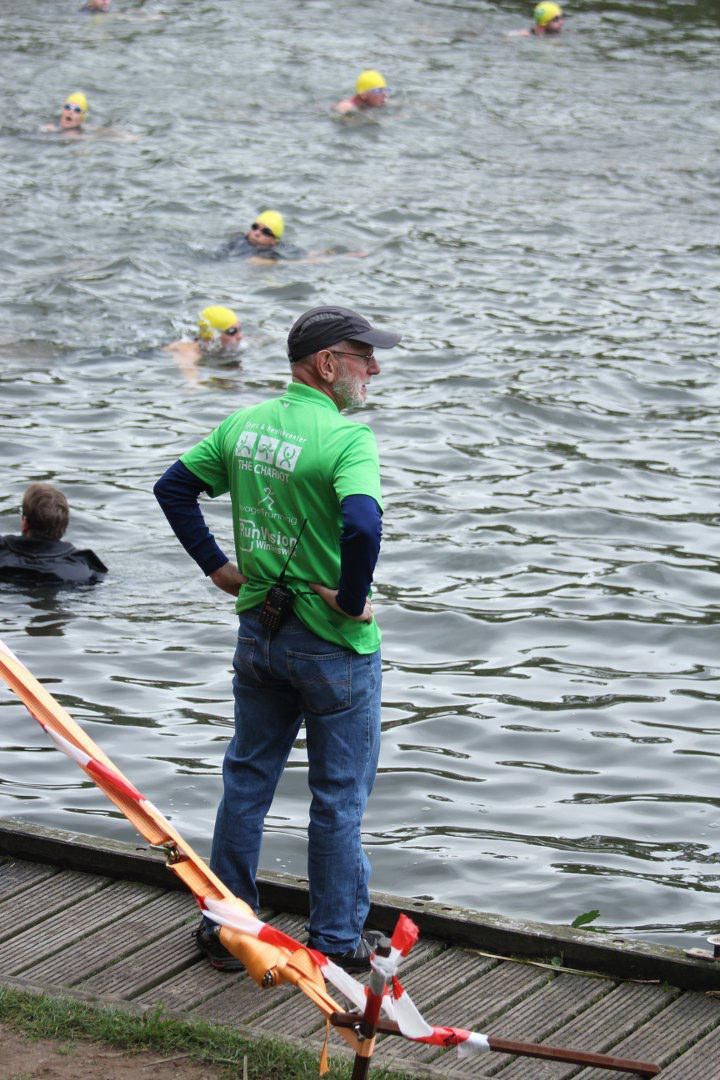 Een man in een groen shirt staat op een steiger en kijkt naar de mensen in het water
