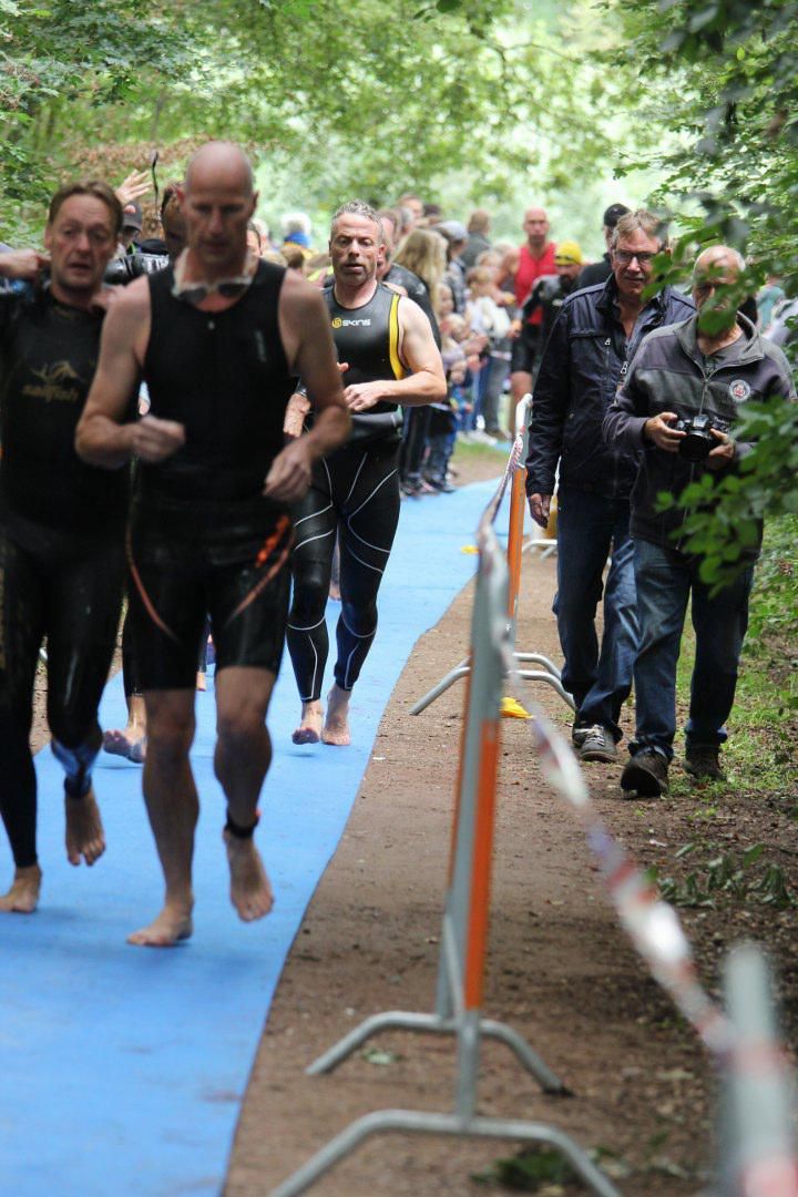 Een groep mannen in wetsuits rent over een pad.
