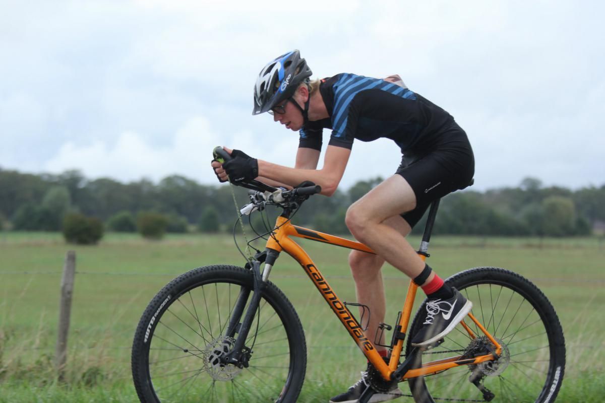 Een man rijdt op een oranje fiets in een veld