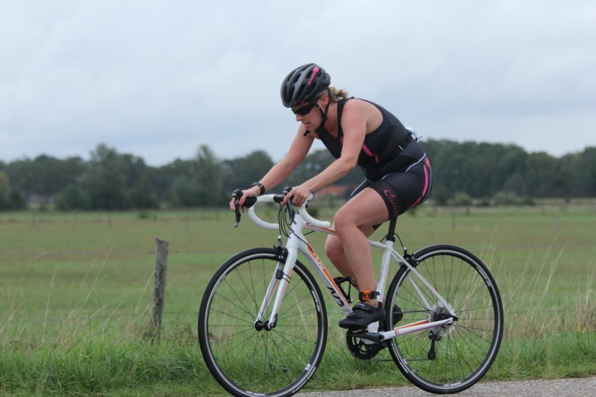 Een vrouw fietst op een weg in een veld.