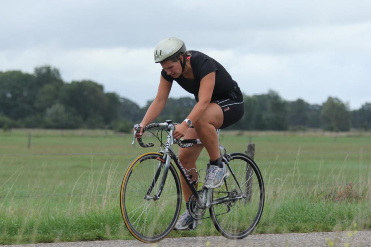 Een vrouw met een helm rijdt op een fiets op een weg