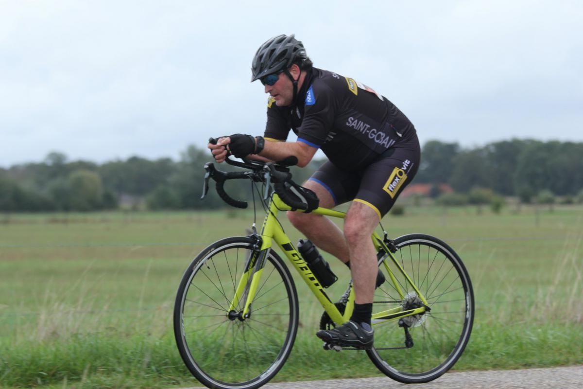Een man rijdt op een gele fiets op een onverharde weg