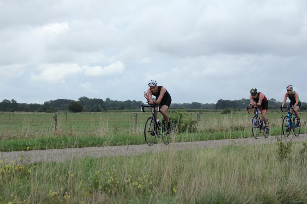 Drie mensen fietsen over een onverharde weg.