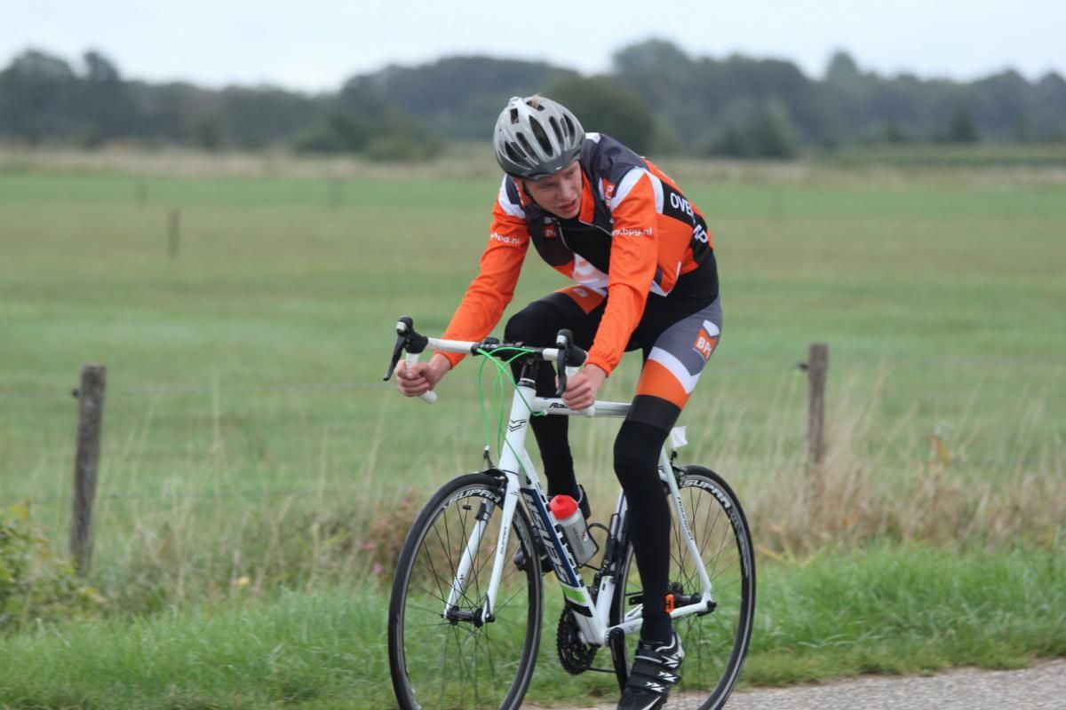 Een man met een helm rijdt op een fiets over de weg.