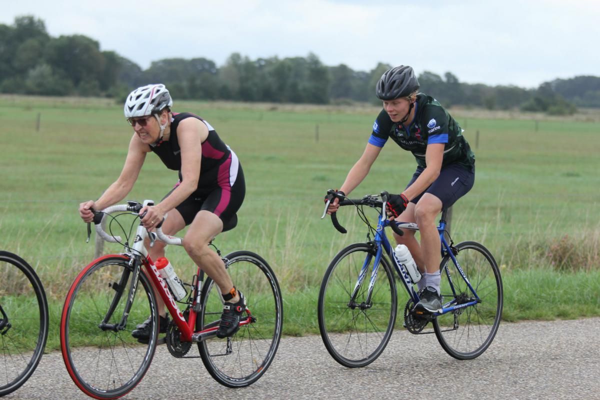 Twee mensen fietsen op een weg in een veld