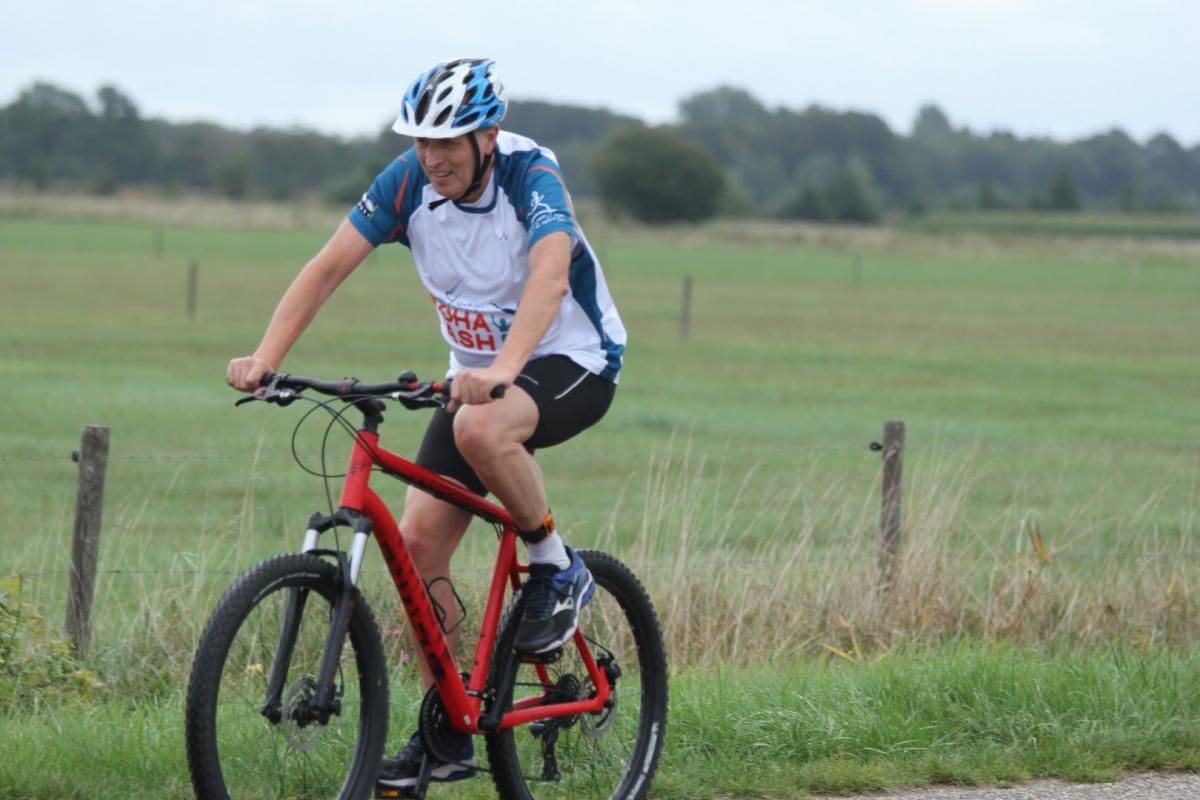 Een man met een helm rijdt op een rode fiets op de weg.