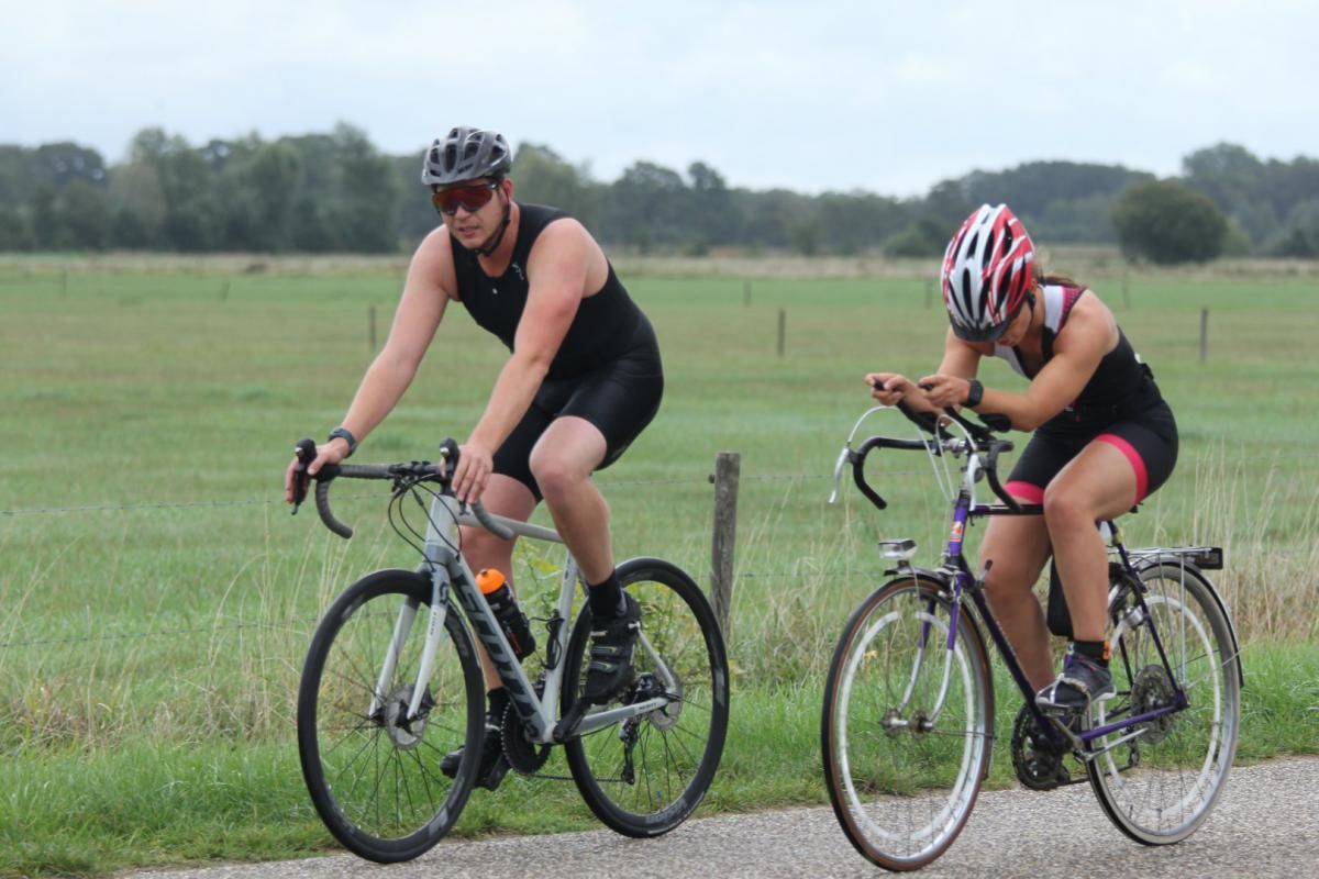 Een man en een vrouw fietsen op een onverharde weg.