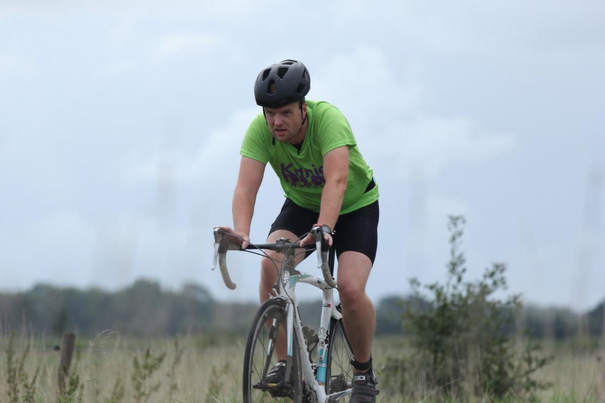 Een man met een helm rijdt op een fiets in een veld.