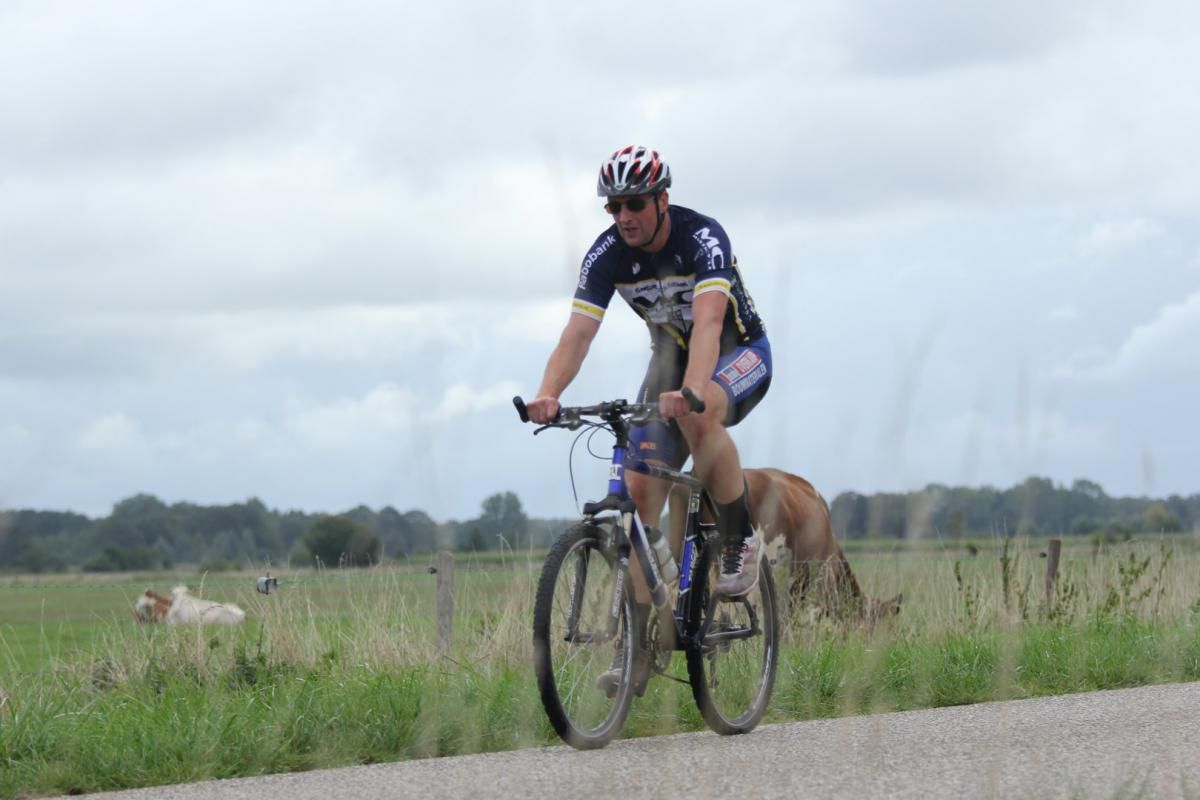 Een man fietst over een weg naast een hond.